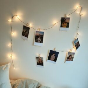 A string of fairy lights with clipped photos on a bedroom wall.