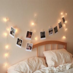 A string of fairy lights with clipped photos on a bedroom wall.